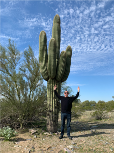man standing next to saguaro imitating with arms up